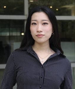 Headshot of Rio, wearing a dark striped shirt and smiling