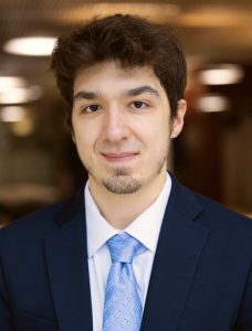 Headshot of Salvatore, wearing a navy suit, white shirt, and light blue tie.