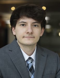Headshot of Anthony, wearing a grey suit and blue plaid tie