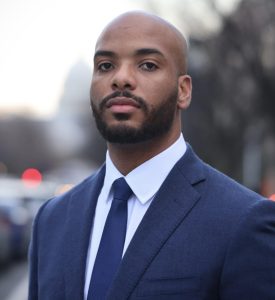 Headshot of Ifeanyi, wearing a navy suit and tie, outside