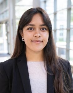 Headshot of Enaya, wearing a light purple shirt and black blazer, smiling