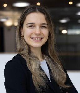 Headshot of Maia, wearing a black blazer and smiling