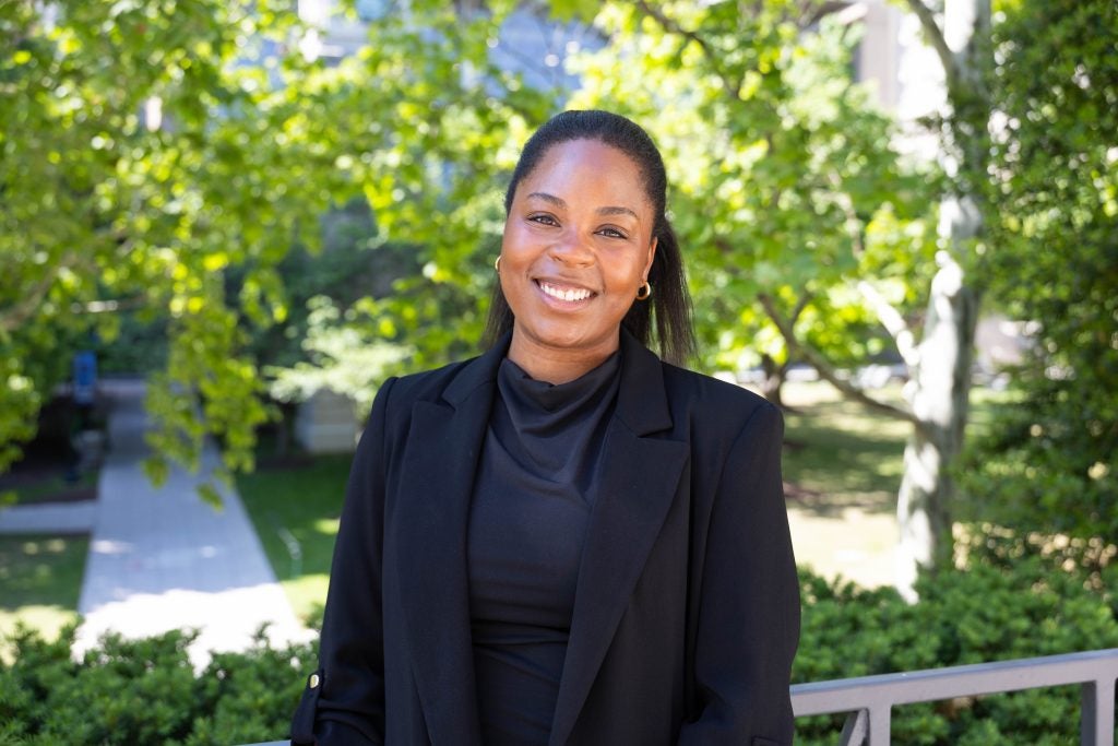 Portrait of a smiling woman in front of greenery on campus