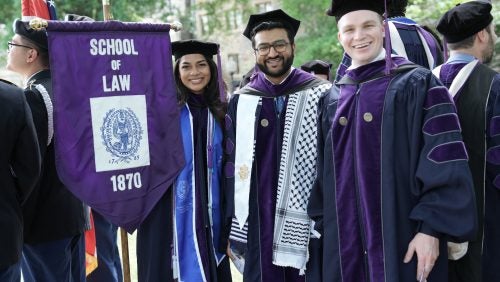 Three graduates in regalia smile and pose for a photo.