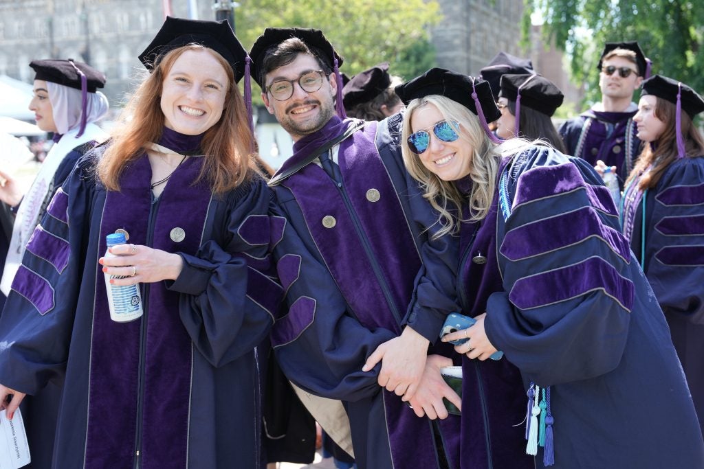 Three graduates in regalia smile and pose.