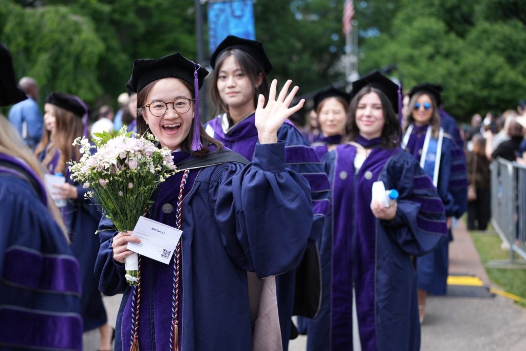 A smiling graduate in regalia holds a bouquet.