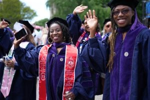 A group of graduates in regalia smile and wave.