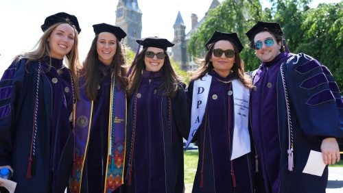 Five graduates smiling in front of Healy Hall.