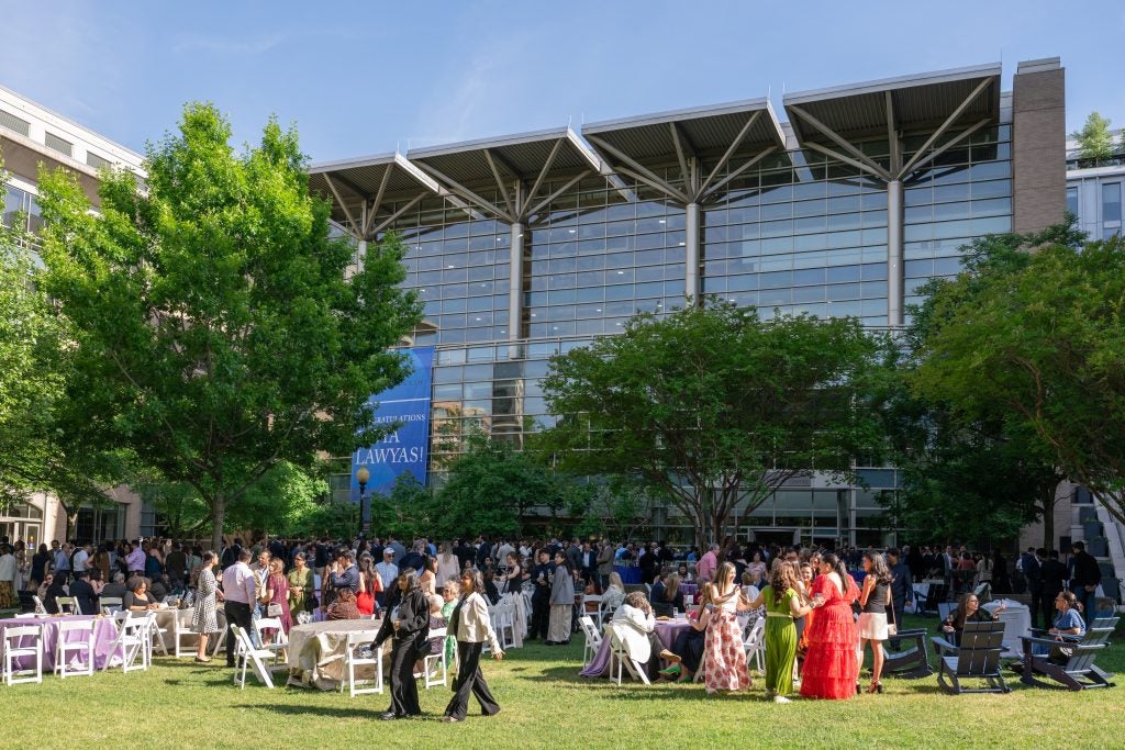A large crowd of graduates and loved ones mingles on the Eleanor Holmes Norton Green.
