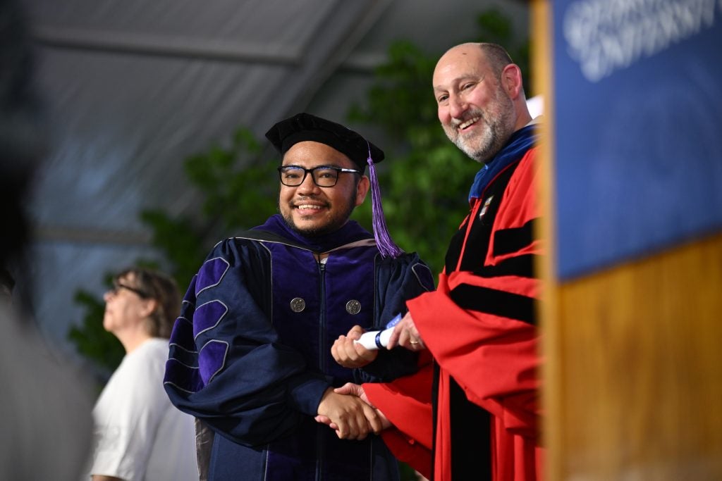 A graduate shakes hands with Interim Dean Teitelbaum as he receives a ceremonial diploma onstage.