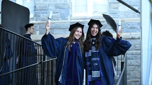 Two graduates smile and pose with their diplomas.