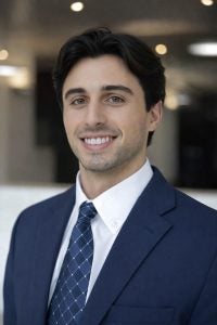 Headshot of Daniel, wearing a navy suit and tie, smiling