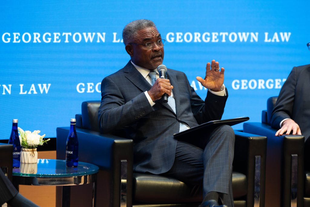 A seated panelist speaks into a microphone as he addresses students. 
