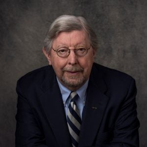 Headshot of a man in a suit and tie wearing glasses