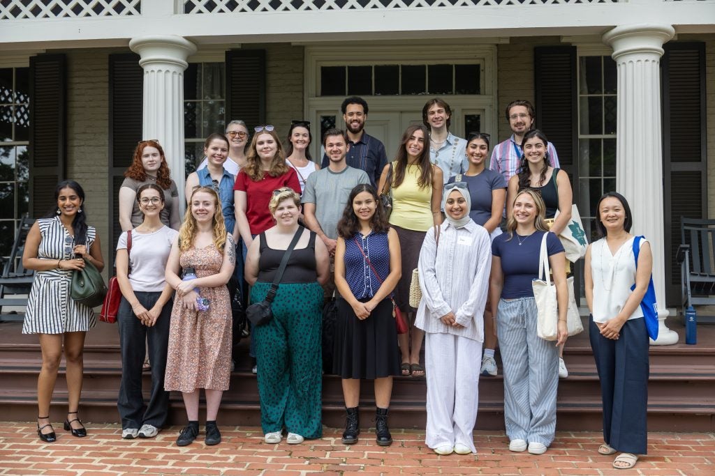 Three rows of smiling students stand on the front steps of a historic home.