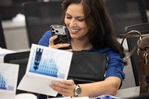 A student with dark hair smiles and takes a photo of a folded greeting card in her hand.