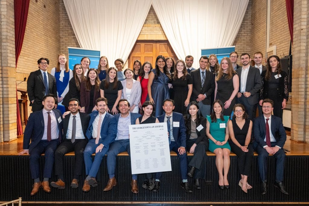 A group of law students together on a stage, holding a poster of the Georgetown Law Journal masthead