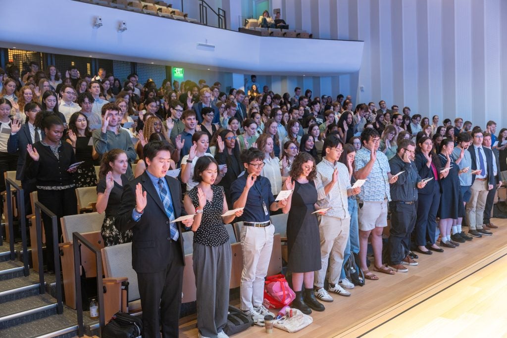 Rows of students stand and raise their right hands while taking an oath