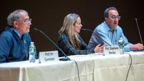 Three professors sit in a row at a table with microphones.