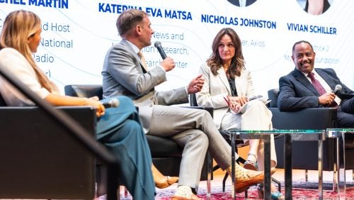 Four people sit onstage and engage in a conversation. See caption for details.