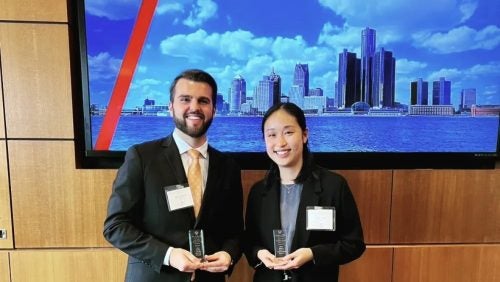 2 students smiling in business attired with awards
