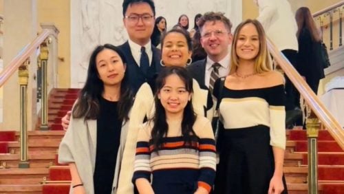 7 students in business attire standing in front of stairs at a competition in vienna