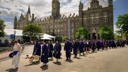 Graduates walking in a line toward Commencement ceremony on a sunny day at Commencement 2025.