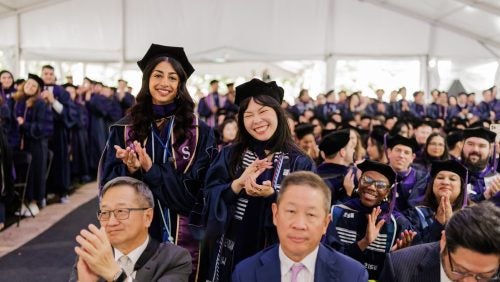 Two students standing in the crowd and applauding at Commencement 2025.