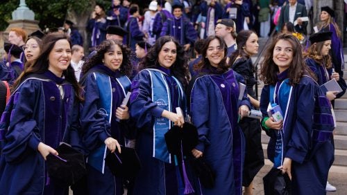 A group of five women pose for a photo by the steps of Healy at Commencement 2025