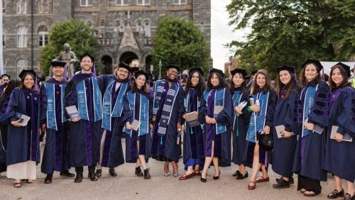 A group of 13 students pose for a photo outside at Commencement 2025